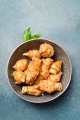 Organic raw Jerusalem artichoke root in a ceramic bowl. On a gray stone background. Close-up. Free space for text.
