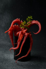 Boiled octopus. Octopus tentacles in a metal can, on a black stone background. Vertical creative photo.