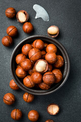 Macadamia nuts in shell. Black ceramic bowl with nuts. Top view. Close-up, on slate background.