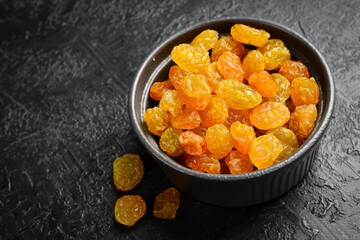 Bowl with dried golden raisins, on a stone background.