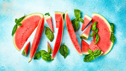 Tropical blue background. Ripe red watermelon slices and green basil. Summer snack concept, top view.