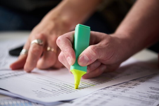 Caucasian middle aged man highlighting financial documents with green marker while Caucasian middle aged woman assisting, both working together on tax paperwork at desk