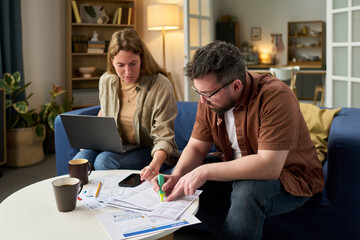 Caucasian young adult woman and Caucasian young adult man reviewing tax documents together at home, man highlighting paperwork while woman using laptop, financial planning concept