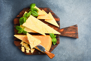 Cheese. Sliced ​​hard aged cheese and basil on a wooden cutting board.