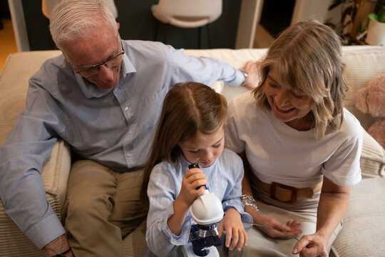 Top view of grandparents and granddaughter learning together, using a microscope to explore scientific curiosity