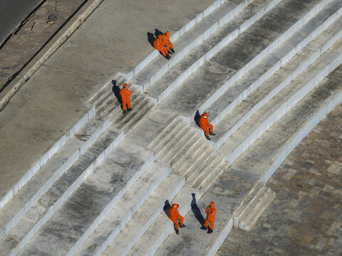 Aerial view of workers in striking orange attire scattered across the concrete steps of a stadium, creating a compelling visual rhythm, Thimphu, Bhutan.