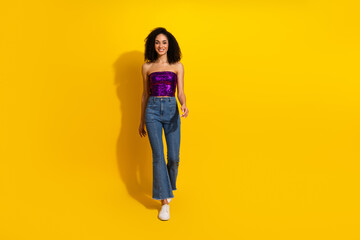 Fototapeta premium Young woman in purple sequin top and jeans posing against bright yellow background for casual fashion lifestyle photography