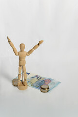 Wooden mannequin celebrating with its arms raised in front of euro banknotes and coins
