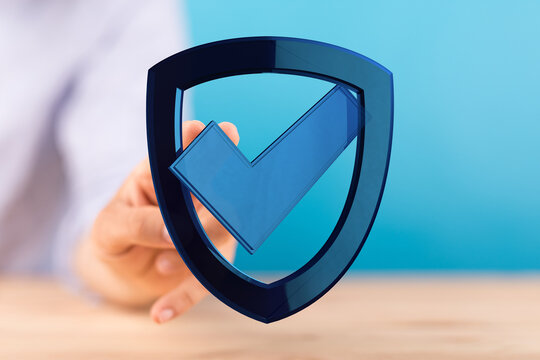 A person holding a blue shield with a checkmark, conveying feelings of safety, reliability, and security in a digital or financial co