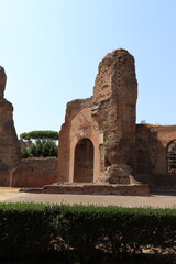 Naklejka premium A dramatic, tall section of ancient Roman bath ruins, featuring a massive brick archway framed by green shrubs