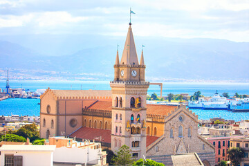 Messina Cathedral in Sicily, Italy, with its distinctive bell tower. Building overlooks the Strait of Messina and a bustling port. Duomo di Messina with prominent clock tower