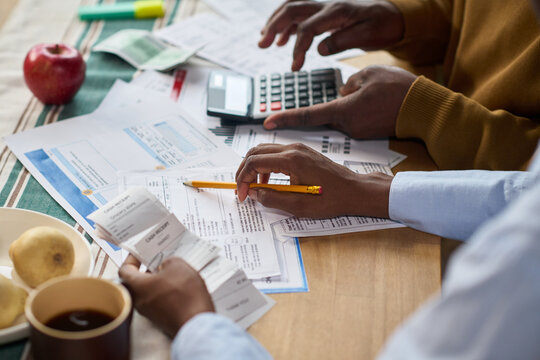 Closeup of Black man and Black woman calculating taxes together at table, reviewing receipts and financial documents with calculator, hands visible holding pencil and paper, coffee and fruit nearby