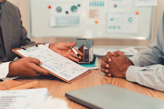 Real estate agent and client sign contract on clipboard on table after signing real estate sales contract along with approved home loan application form.