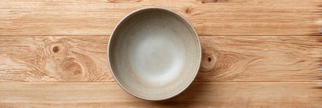 Empty ceramic bowl with rustic minimalist feel, seen from an overhead view on wooden kitchen table. tranquil, simple scene evoking sense of calm waiting