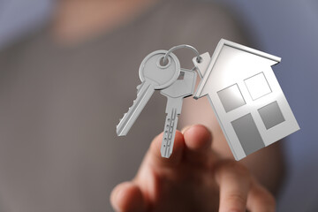 Close-up of a hand presenting a set of keys and a house-shaped pendant, symbolizing home, ownership, and new beginnings. Ideal for real estate a