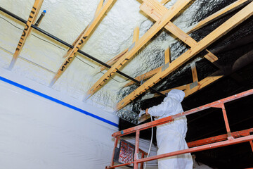 Worker applies paint over foam insulation to wooden beams in renovation, enhancing energy efficiency