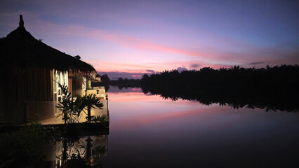 Fototapeta premium Resort bungalows reflecting colorful sunrise sky over River Tha Sathon, Surat Thani, Thailand, Southeast Asia.