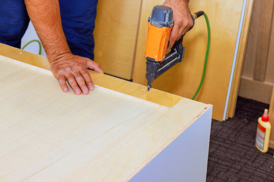 Carpenter uses nail gun on piece of wood, working on furniture assembly