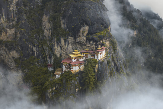 Aerial view of the majestic Tiger's Nest monastery clinging to the cliffside, shrouded in ethereal mist, a testament to spiritual devotion, Paro, Bhutan.