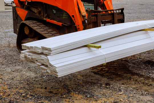 Heavy machinery transports long white wooden beams at busy construction site