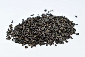 Dry black tea leaves lie in a pile on a white background.