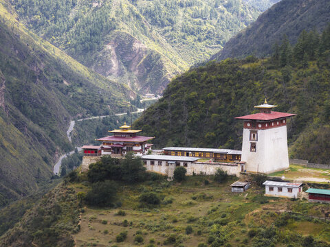 Aerial view of traditional Bhutanese Dobji Dzong merges with the rugged mountain landscape, where a serene river carves its path through the valley, Raga, Paro, Bhutan.