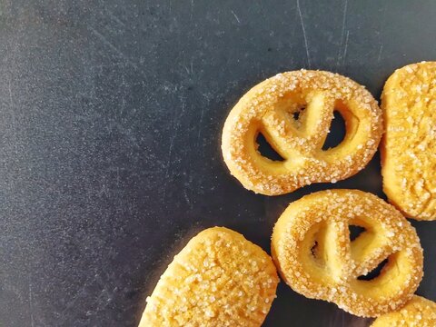 Assorted Danish butter cookies with sugar sprinkles on dark background. Delicious shortbread biscuits in various shapes (pretzel, round, rectangle) for holiday treats and sweet dessert concepts.