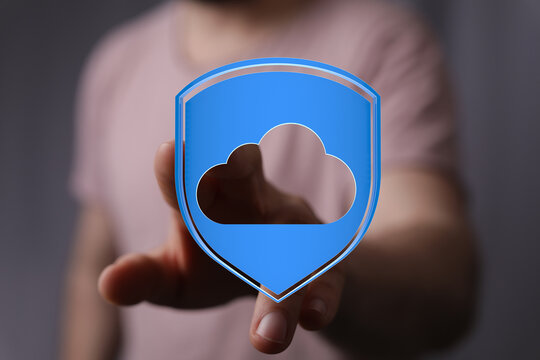 Hand reaching out to touch a cloud shield icon representing data protection, security, and cloud storage. Conce
