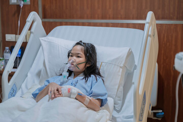 Sick Asian girl wearing oxygen mask lying on hospital bed receiving treatment. Healthcare concept,...