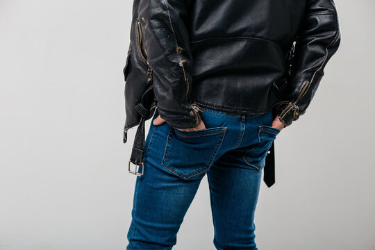 a tough guy in classic jeans and an old leather jacket is standing with his back turned, his hands in the back pockets of his jeans. male ass in close-up