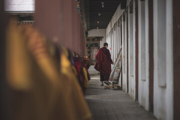 Gangtey Monastery, Bhutan - 20 September 2025: View of a monk walking along the corridor, his maroon robe a stark contrast to the white walls and colorful fabrics.