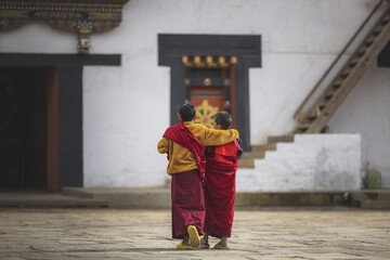 Gangtey, Bhutan - 20 September 2025: View of two young monks in vibrant saffron robes walking together in front of the Gangtey Monastery, a serene blend of white walls and dark wooden accents.