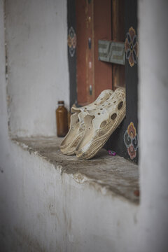 Gangtey Monastery, Bhutan - 20 September 2025: View of worn, weathered shoes resting on a stone windowsill, a small bottle beside them, against the backdrop of intricately painted woodwork.