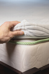 Hand is touching white soft mattress. Topper mattress with a core of pressure-relieving gel foam. Adapts to body and leads away excess heat. Vertical photo.