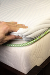 Hand is touching very soft orthopedic topper mattress. Vertical photo.