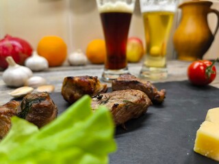 Delicious pieces of shish kebab lie on a sliced board. There are glasses of dark and light beer in the background.