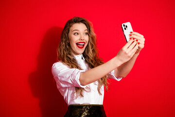 Happy young woman taking selfie with phone in trendy outfit on red background showcasing joyful...
