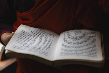 View of crimson robes and a book open, revealing intricate script, creating a serene moment of study and reflection, Wolakha, Punakha, Bhutan.