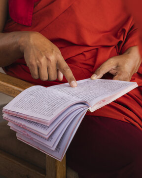 View of a monk's aged hands guide the reader through ancient script, a vibrant splash of crimson robes against the crisp pages, Wolakha Nunnery, Punakha, Bhutan.