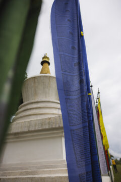 View of vibrant prayer flags fluttering beside a white stupa with a golden spire, under a serene sky, Wolakha Nunnery, Punakha, Bhutan.