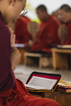 View of monks in vibrant red robes chanting from sacred texts, their devotion palpable in the tranquil air, Wolakha Nunnery, Punakha, Bhutan.
