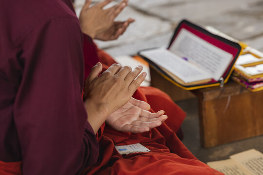 View of hands clapping, the scene radiates a sense of devotion and tradition, the rich red robes contrast with the open book, Wolakha Nunnery, Punakha, Bhutan.