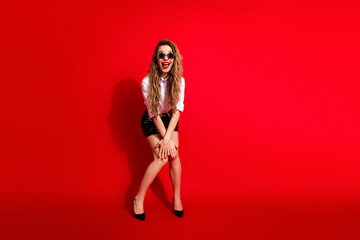 Young woman in fashionable outfit standing confidently with red background, exhibiting elegance and...