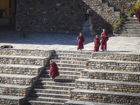 Haa, Bhutan - 26 September 2025: Aerial view of monks in vibrant maroon robes descending the stone steps of Haa Dzong, a play of light and shadow on ancient textures.