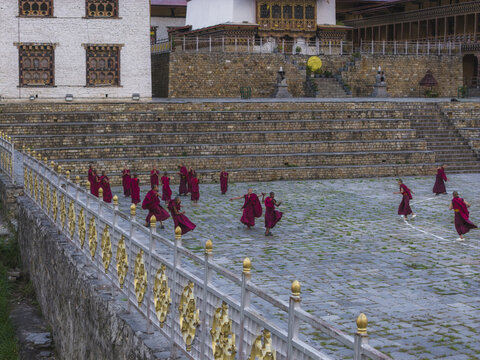 Haa, Bhutan - 25 September 2025: Aerial view of the Haa Dzong courtyard where monks in vibrant maroon robes dance, their forms a striking contrast against the pale stone paving.