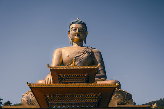 View of the golden Buddha Dordenma statue sits serenely against a clear blue sky, the elaborate details of its design highlighted by the sun, Thimphu, Bhutan.