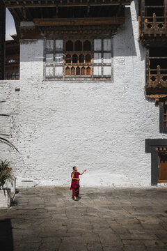 Trongsa, Bhutan - 22 September 2025: View of a lone figure in vibrant red stands against the stark white walls of Trongsa Dzong, its intricate wooden windows casting deep shadows in the courtyard.