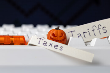 halloween pumpkin toy on computer keyboard with paper labels reading "taxes" and "tariffs," symbolizing fear, costs, and economic burdens