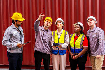 Happy diverse group of engineers workers checking inventory with tablet device in the container yard background. This is a freight transportation and distribution warehouse.