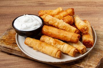 fried spring rolls with cheese, on a wooden background, with cream sauce, no people,